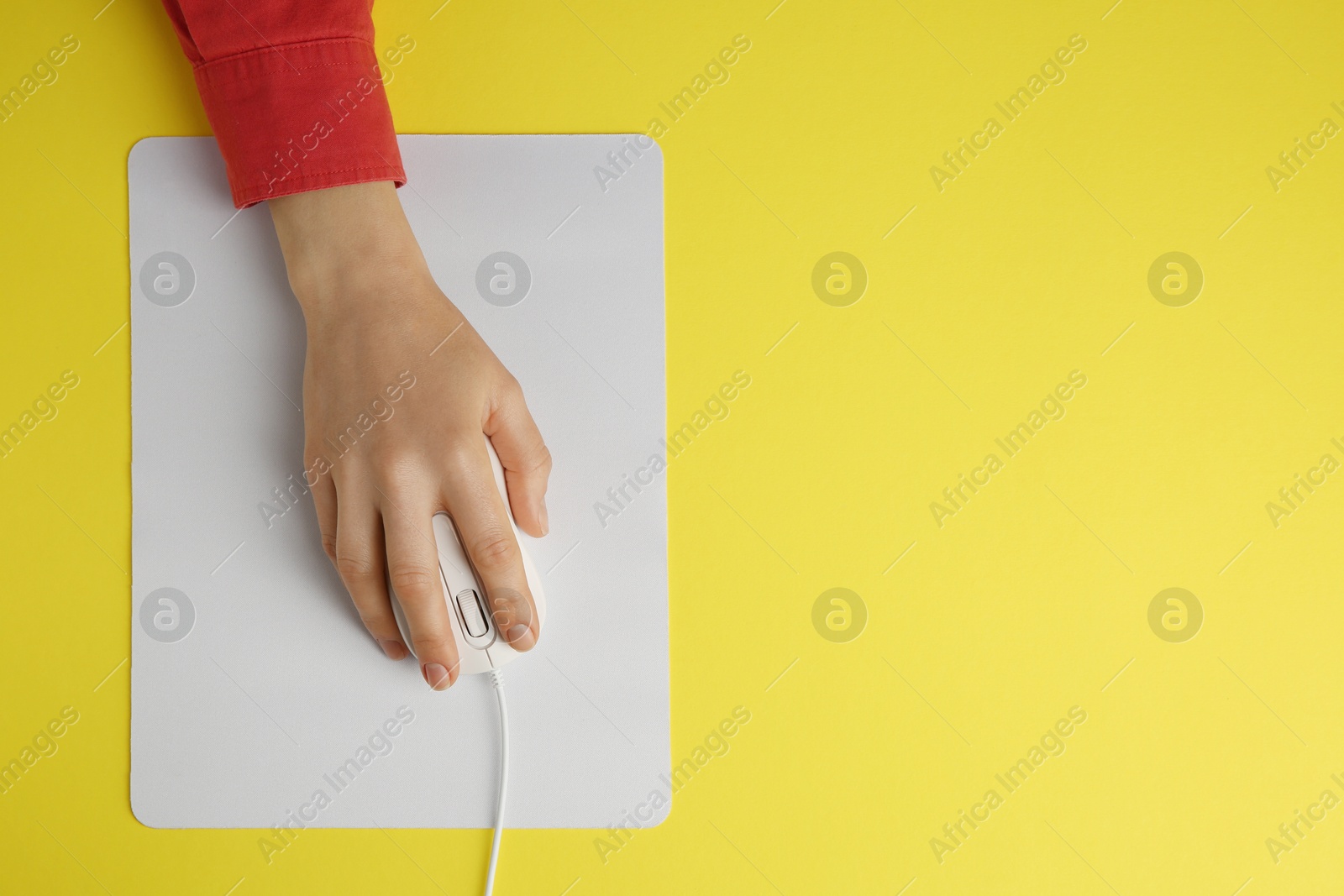 Photo of Woman using modern wired computer mouse on yellow background, top view. Space for text