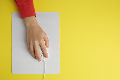 Photo of Woman using modern wired computer mouse on yellow background, top view. Space for text