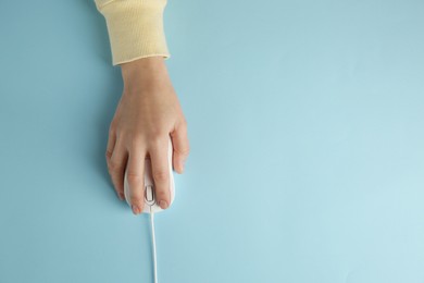 Photo of Woman using modern wired computer mouse on light blue background, top view. Space for text