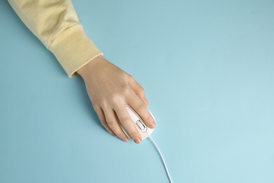 Photo of Woman using modern wired computer mouse on light blue background, top view. Space for text
