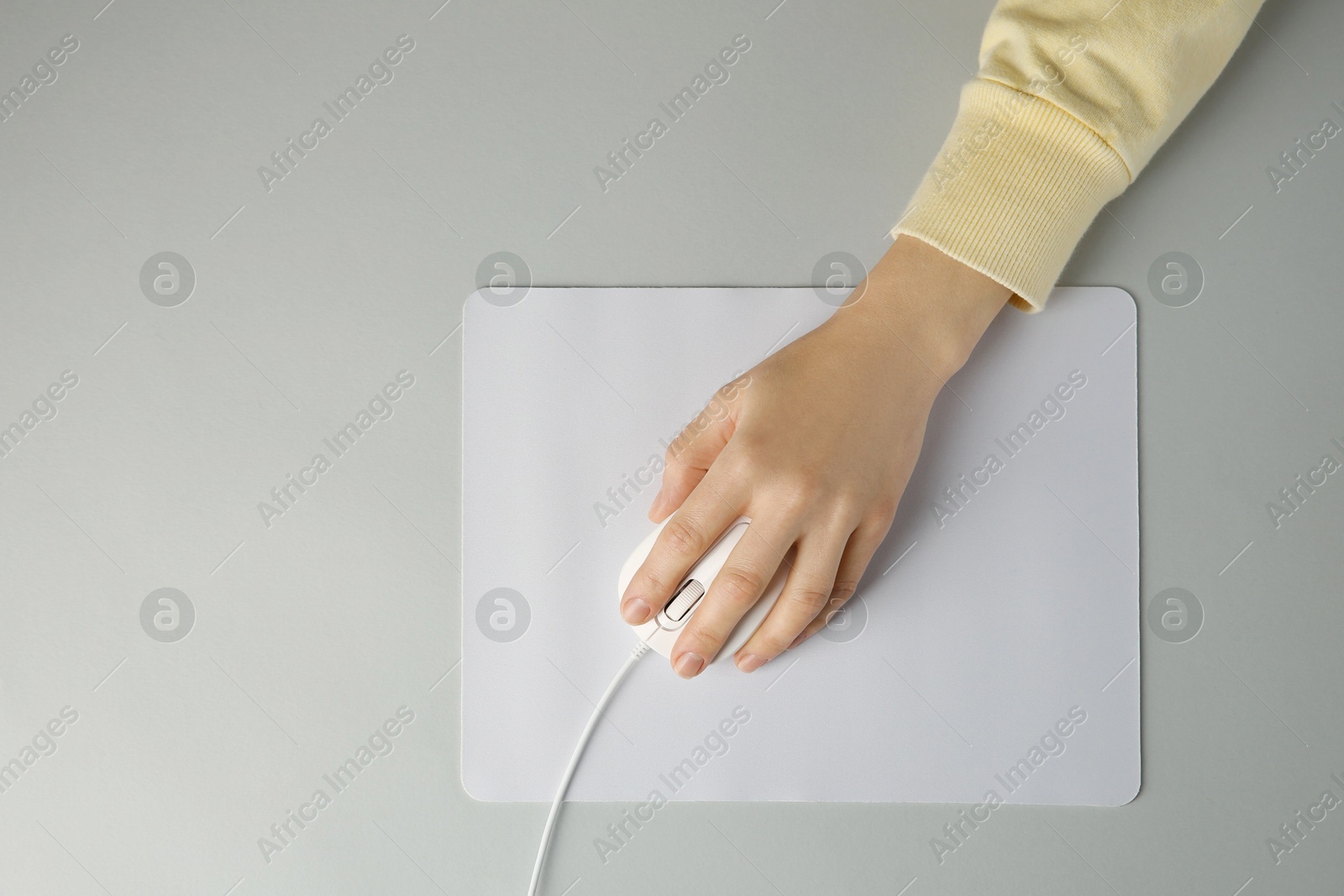 Photo of Woman using modern wired computer mouse on grey background, top view. Space for text