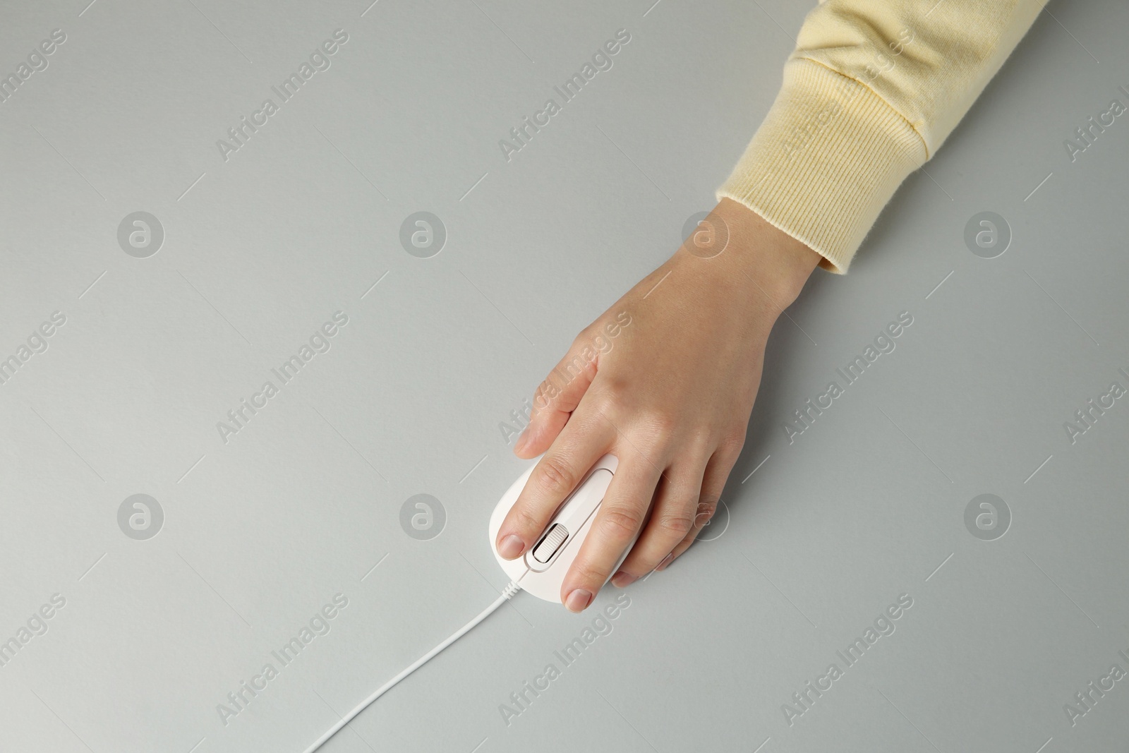 Photo of Woman using modern wired computer mouse on grey background, top view. Space for text