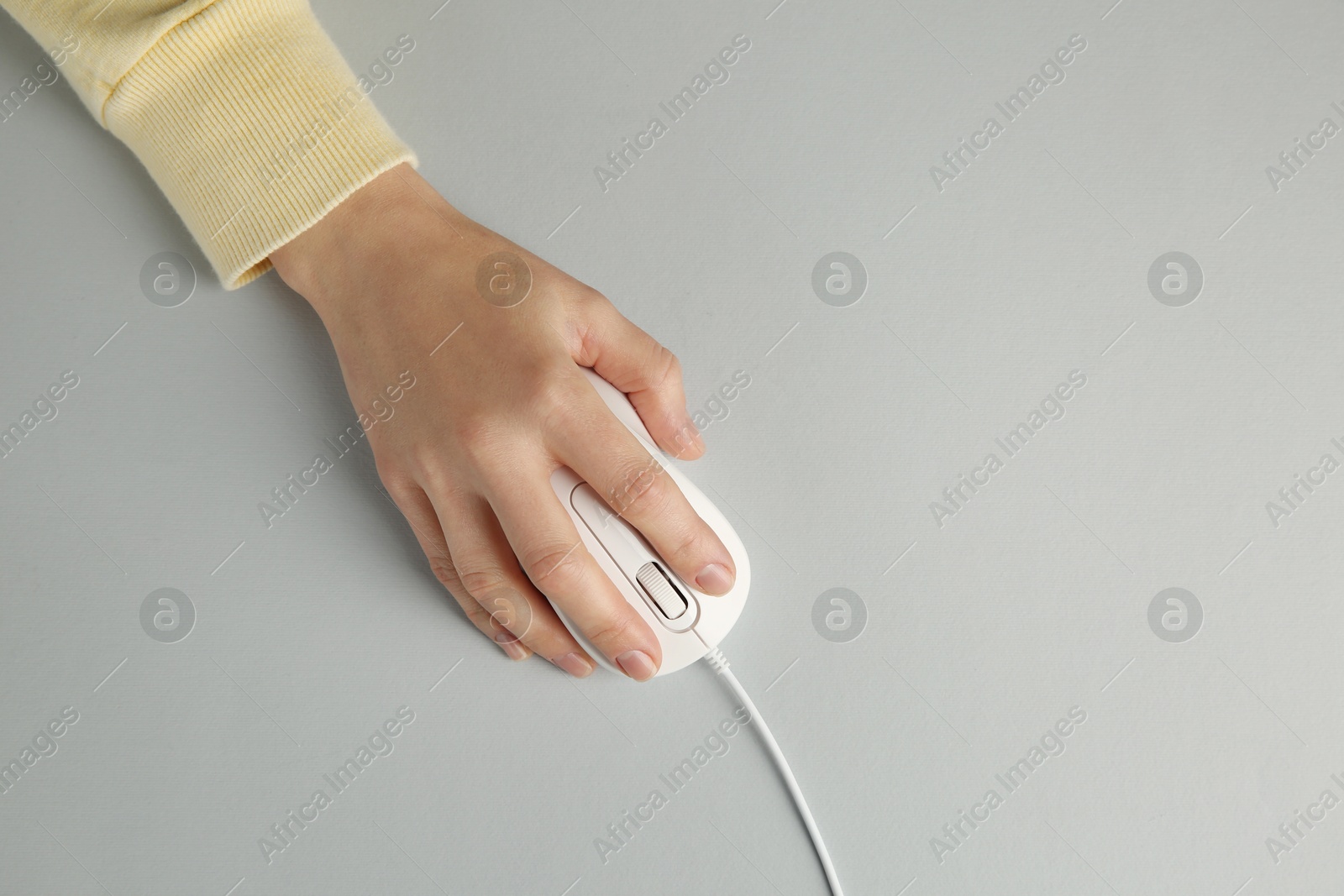 Photo of Woman using modern wired computer mouse on grey background, top view. Space for text