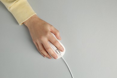 Photo of Woman using modern wired computer mouse on grey background, top view. Space for text