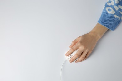 Photo of Woman using modern wired computer mouse on light background, top view. Space for text