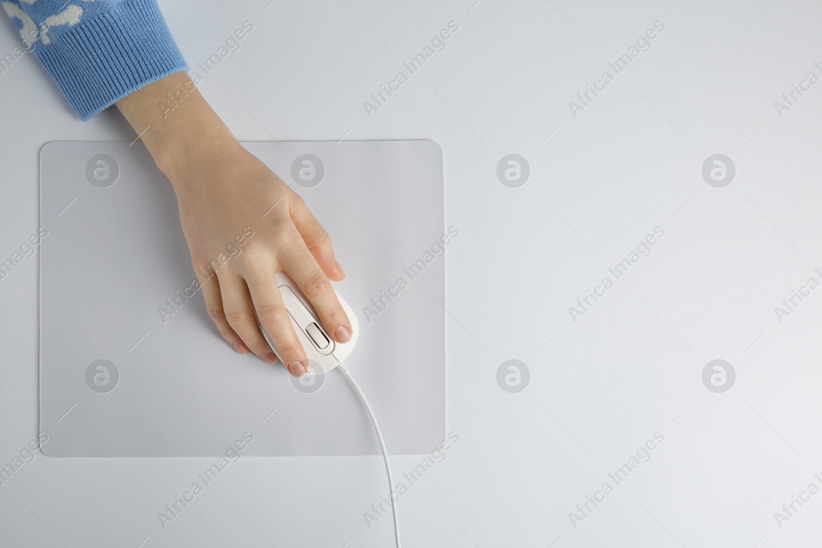 Photo of Woman using modern wired computer mouse on light background, top view. Space for text