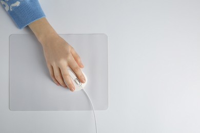 Photo of Woman using modern wired computer mouse on light background, top view. Space for text