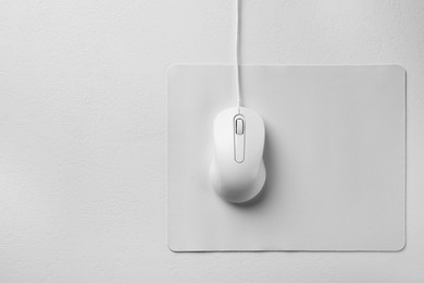 Wired mouse with mousepad on light textured table, top view. Space for text