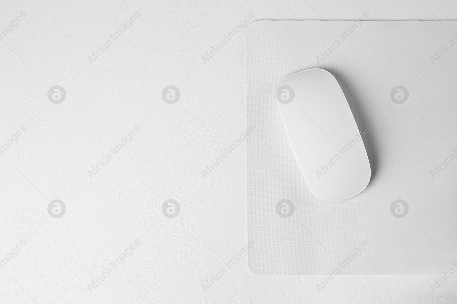 Photo of One wireless mouse with mousepad on light textured table, top view. Space for text