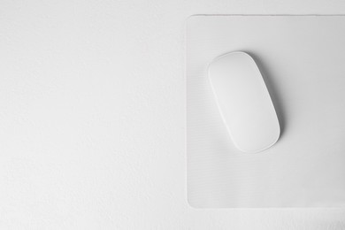 Photo of One wireless mouse with mousepad on light textured table, top view. Space for text