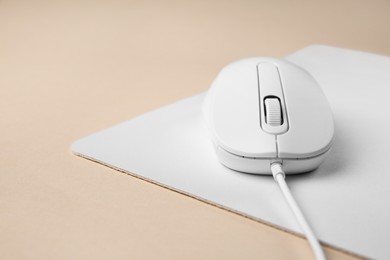Wired mouse with mousepad on beige background, closeup. Space for text