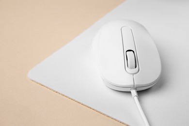 Wired mouse with mousepad on beige background, closeup. Space for text