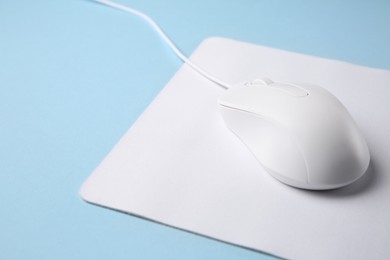 Wired mouse with mousepad on light blue background, closeup