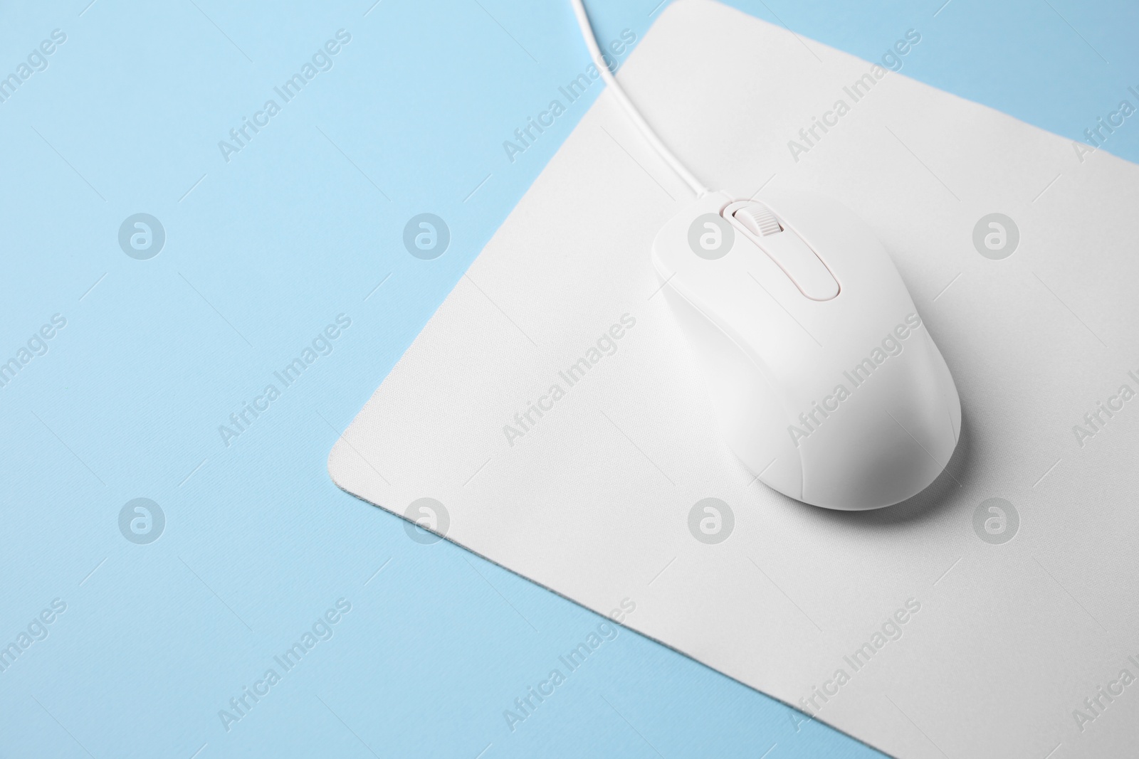 Photo of Wired mouse with mousepad on light blue background. Space for text