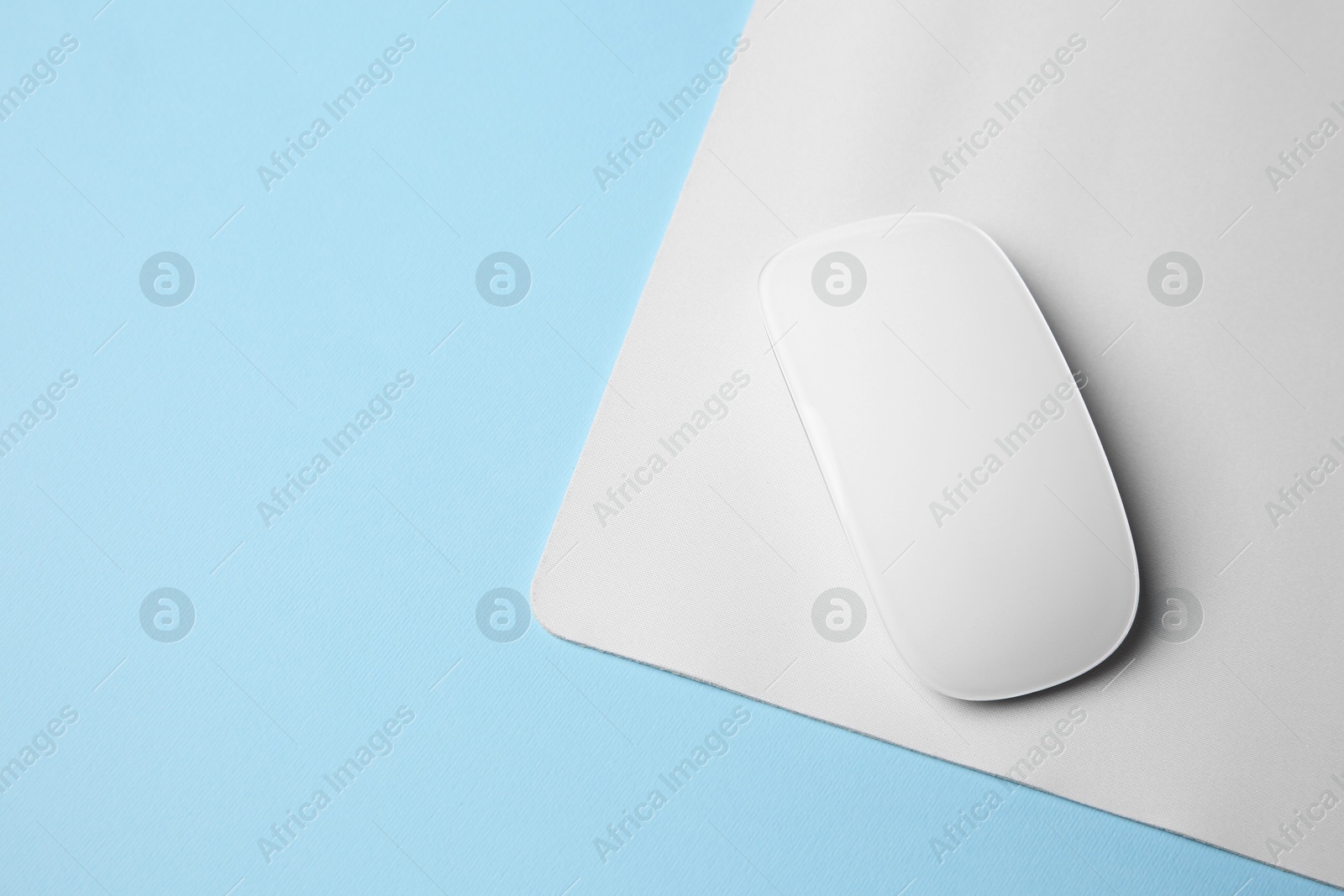 Photo of One wireless mouse with mousepad on light blue background, top view. Space for text