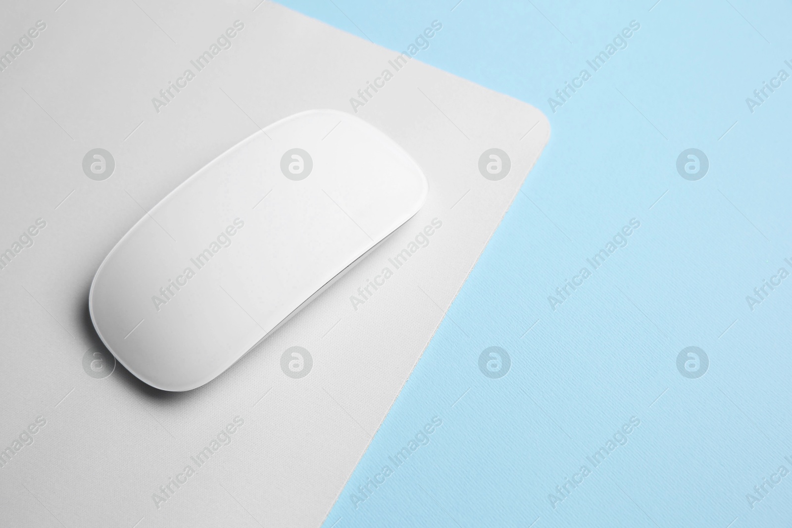 Photo of One wireless mouse with mousepad on light blue background, above view. Space for text