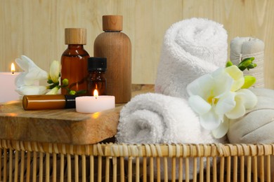 Aromatherapy products and burning candles in wicker basket, closeup