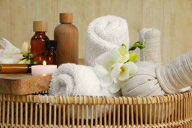 Photo of Aromatherapy products and burning candle in wicker basket, closeup
