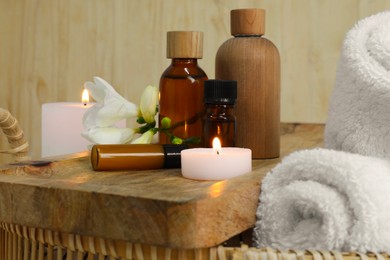 Photo of Aromatherapy products and burning candles in wicker basket, closeup
