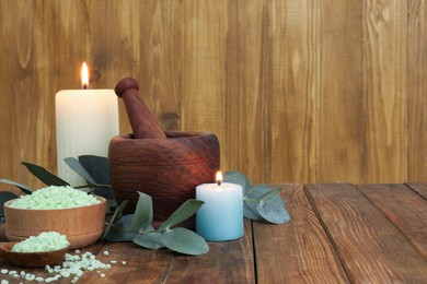 Aromatherapy products, burning candles and eucalyptus leaves on wooden table, space for text