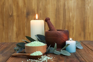 Aromatherapy products, burning candles and eucalyptus leaves on wooden table