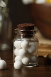 Photo of Homeopathy. Pills in glass bottle on wooden table, closeup