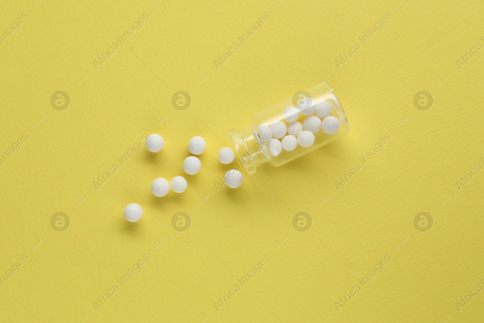 Photo of Bottle with homeopathic remedy on yellow background, top view