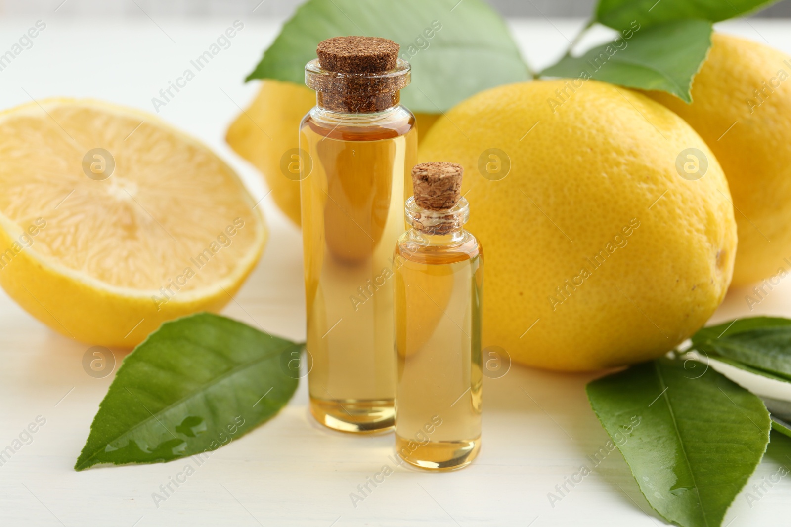 Photo of Essential oils in bottles, lemons and green leaves on white table, closeup