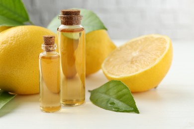 Essential oils in bottles, lemons and green leaves on white table, closeup