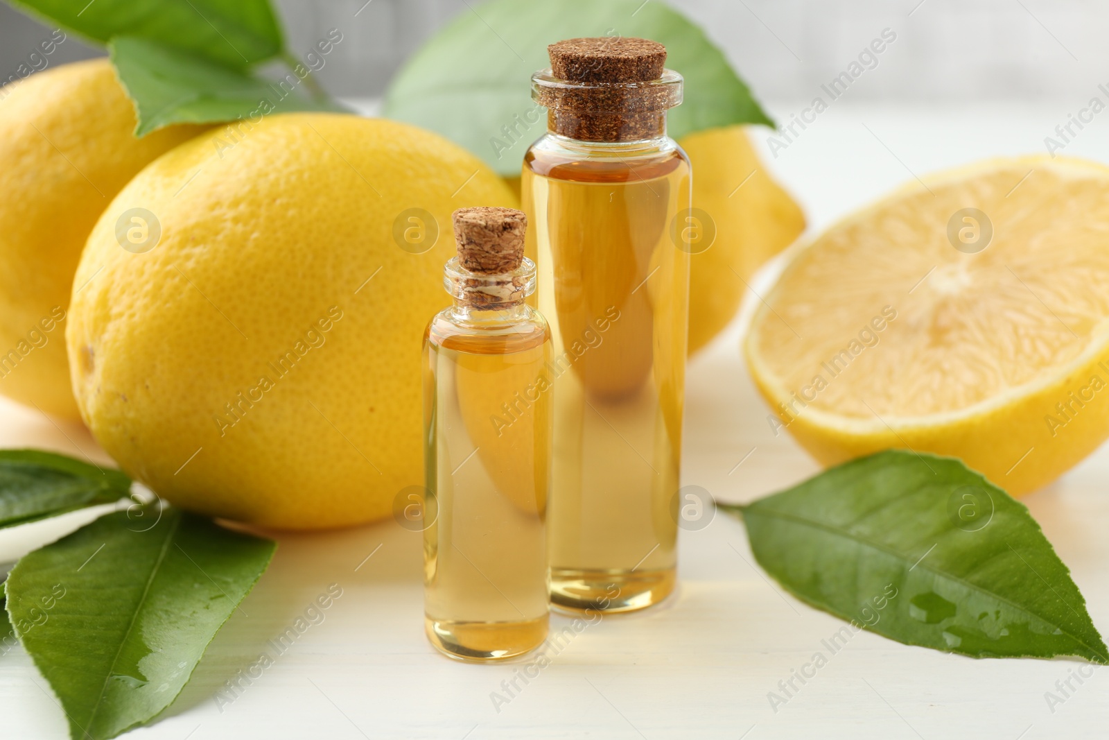 Photo of Essential oils in bottles, lemons and green leaves on white table, closeup