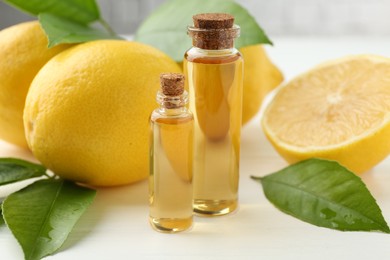 Photo of Essential oils in bottles, lemons and green leaves on white table, closeup