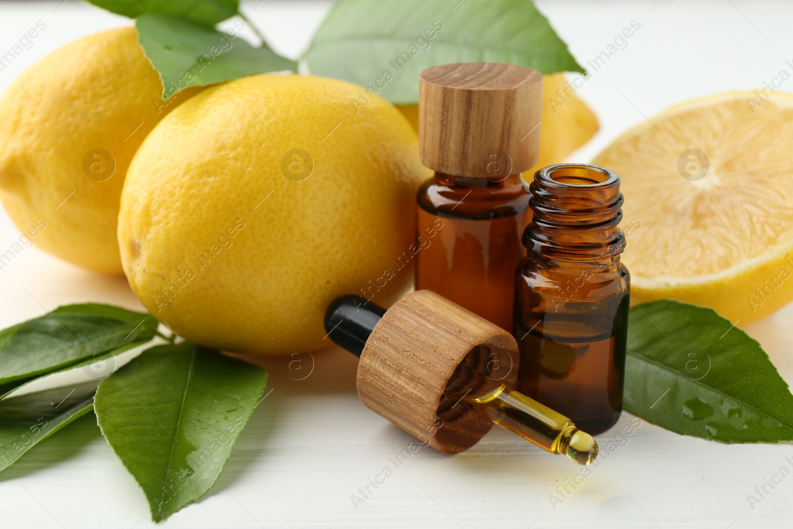 Photo of Essential oils in bottles, dropper, lemons and green leaves on white table, closeup