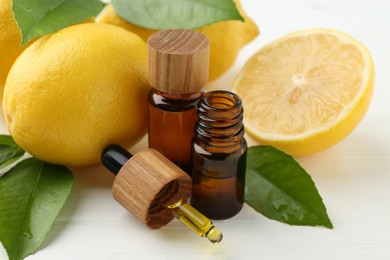 Essential oils in bottles, dropper, lemons and green leaves on white table, closeup