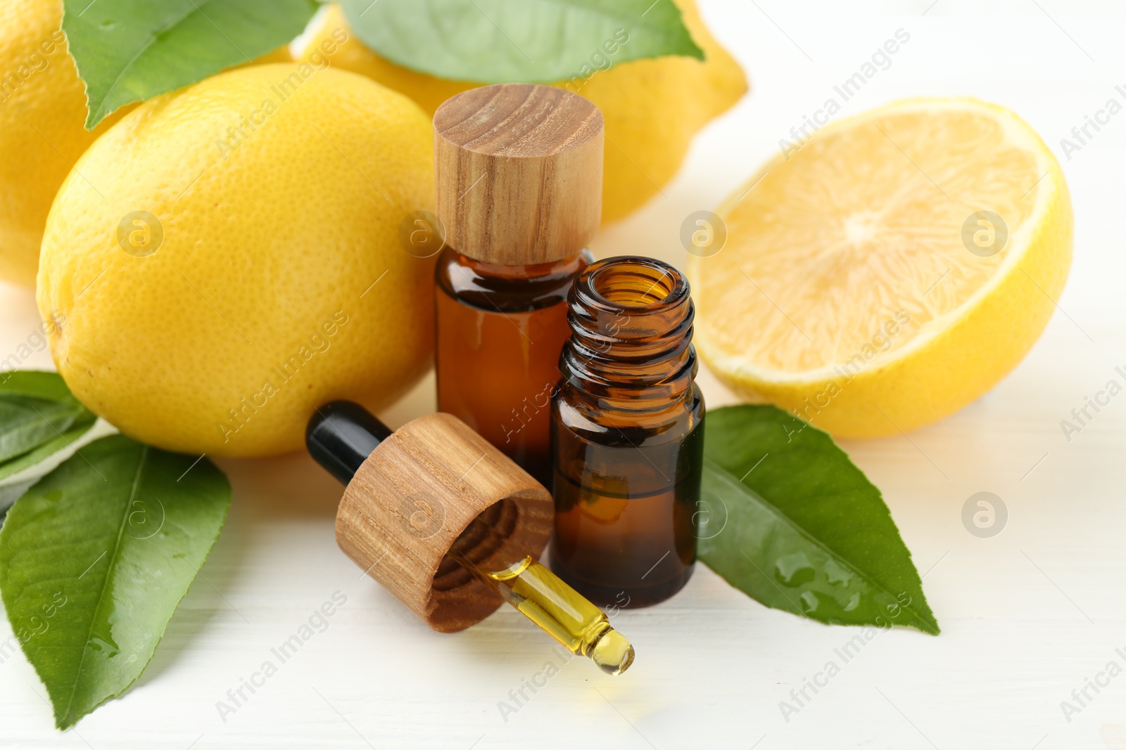 Photo of Essential oils in bottles, dropper, lemons and green leaves on white table