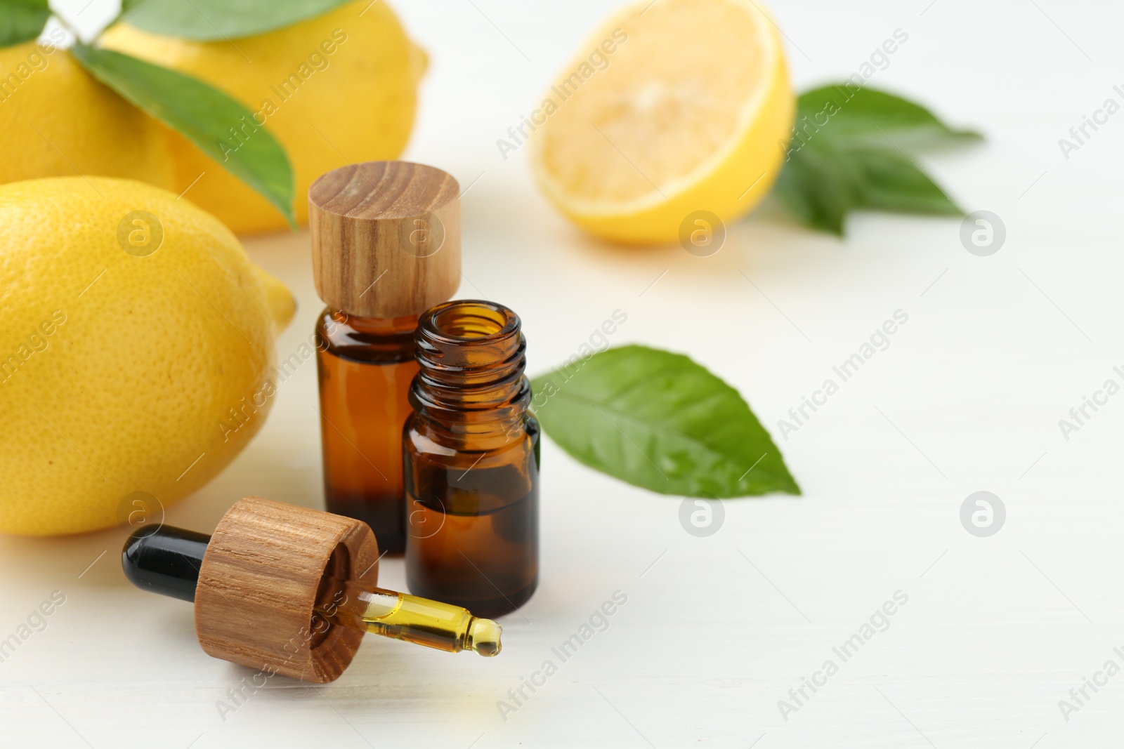 Photo of Essential oils in bottles, dropper, lemons and green leaves on white table