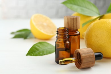 Essential oils in bottles, dropper, lemons and green leaves on white table