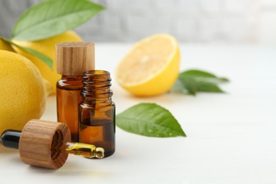 Photo of Essential oils in bottles, dropper, lemons and green leaves on white table