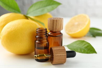 Photo of Essential oils in bottles, dropper, lemons and green leaves on white table