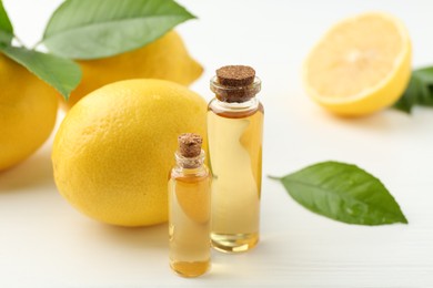 Photo of Essential oils in bottles, lemons and green leaves on white table