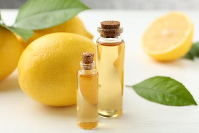 Essential oils in bottles, lemons and green leaves on white table, closeup