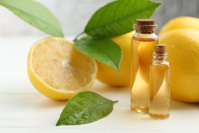 Photo of Essential oils in bottles, lemons and green leaves on white table