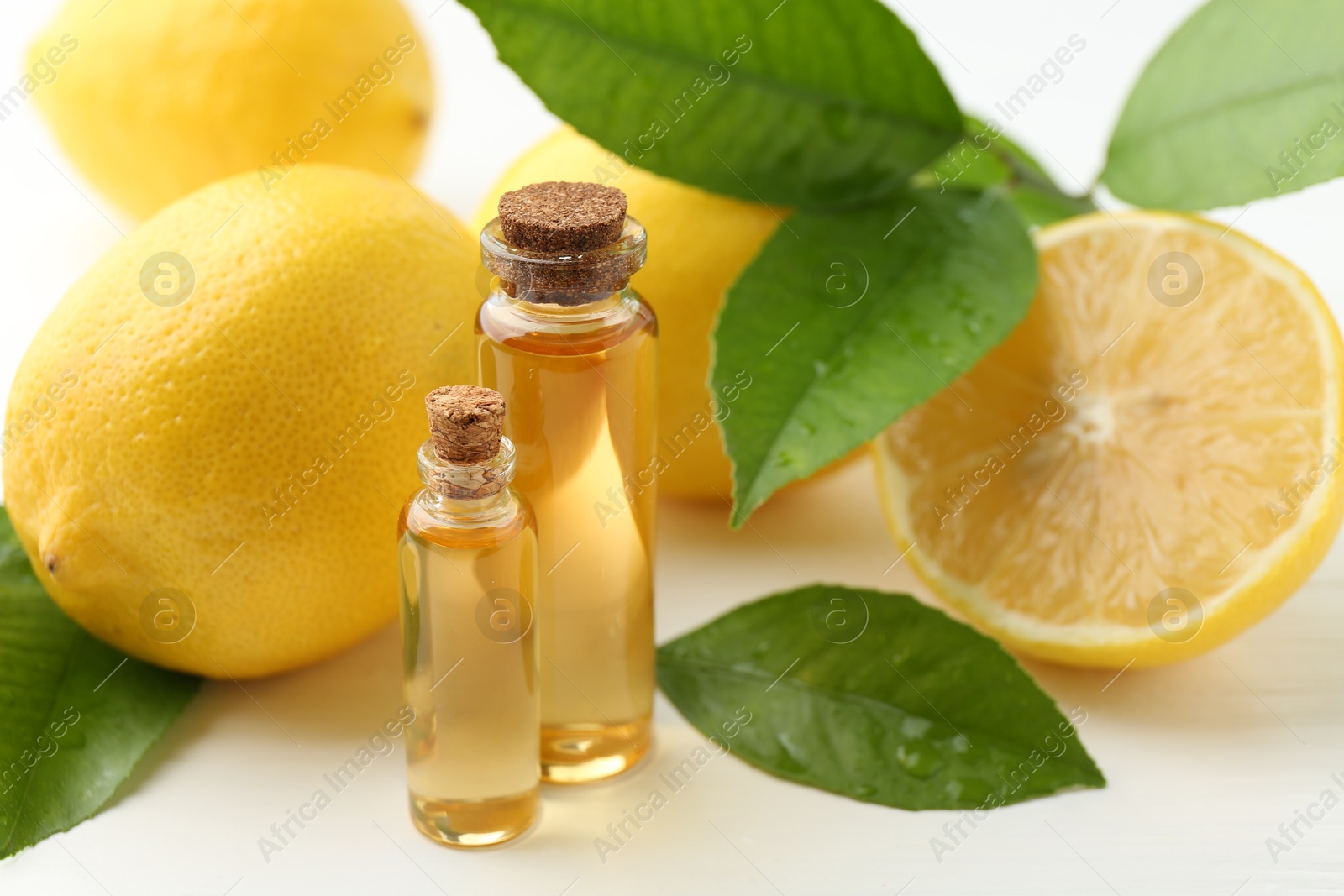 Photo of Essential oils in bottles, lemons and green leaves on white table