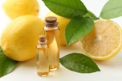 Essential oils in bottles, lemons and green leaves on white table