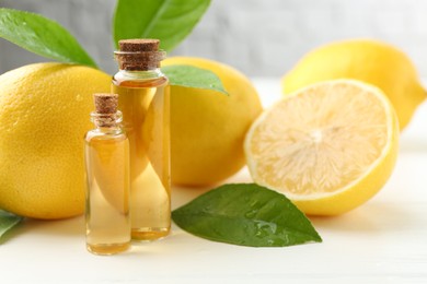 Essential oils in bottles, lemons and green leaves on white table