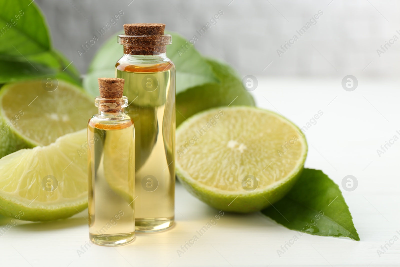 Photo of Essential oils in bottles, limes and green leaves on white table, closeup