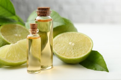 Essential oils in bottles, limes and green leaves on white table, closeup