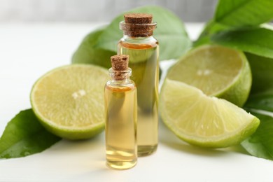 Photo of Essential oils in bottles, limes and green leaves on white table, closeup