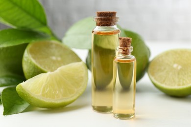 Photo of Essential oils in bottles, limes and green leaves on white table, closeup