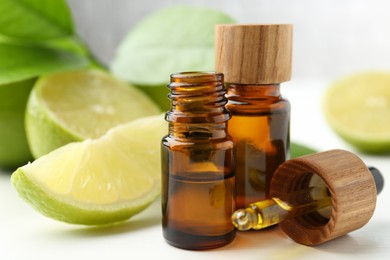 Essential oils in bottles, dropper and limes on white table, closeup