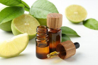 Essential oils in bottles, dropper, limes and green leaves on white table, closeup